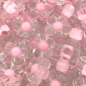 May include: A pile of clear plastic flower-shaped beads with pink centers. The beads are translucent and have a glossy finish.