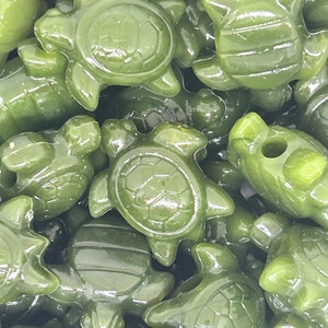 May include: A close-up of a group of green turtle-shaped beads. The beads are made of a smooth, glossy material and have a realistic turtle design.