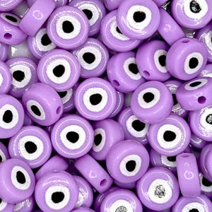 May include: A pile of light purple beads, each featuring a white and black eye motif. The beads are a mix of round and cylindrical shapes, with a shiny surface. These beads are suitable for jewellery making and craft projects.