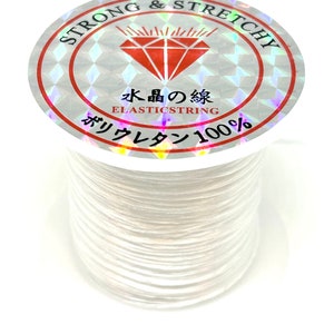 Pu&ograve; includere: Filo elastico bianco su una bobina con un'etichetta che recita "Strong & Stretchy" e "Elastic String 100%" in giapponese.
