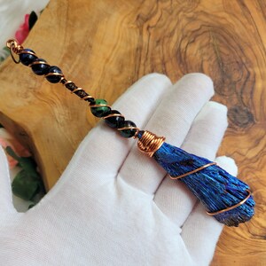 May include: A blue and green crystal wrapped in copper wire, with black and green beads on a copper wire, forming a pendant or charm.