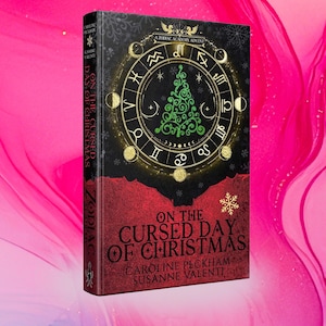 May include: A hardcover book titled On the Cursed Day of Christmas by Caroline Peckham and Susanne Valenti. The black cover features a gold zodiac wheel surrounding a green swirling Christmas tree graphic, with red accents at the bottom.
