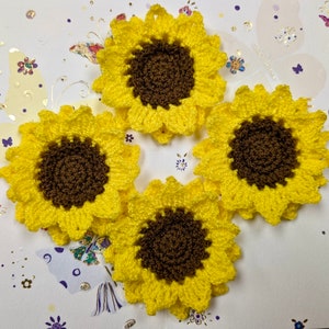 May include: Four crocheted yellow sunflowers with brown centers. The sunflowers are arranged in a circle on a white background.