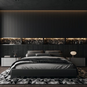 Op de afbeelding: Een zwart bed met een grijs dekbed en zwarte kussens staat in een donkere slaapkamer met een zwart hoofdbord en een zwart-wit gestreept tapijt. Het hoofdbord heeft een ingebouwde plank met een marmeren achterwand en een klein lampje op een nachtkastje.