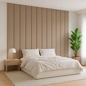May include: A modern bedroom with a beige upholstered headboard. The bed is made with white bedding and pillows. A wooden nightstand with a lamp sits to the left of the bed. A large potted plant is on the right side of the bed.