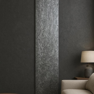 May include: A vertical, textured, gray stone panel against a dark gray wall. The panel is the focal point, with a sofa, lamp, and wooden table in the background, creating a modern interior design aesthetic.