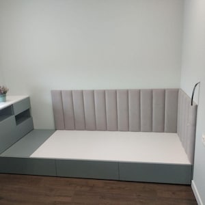 May include: A modern bed frame with a gray headboard and a white mattress. The bed is built into a corner, with a matching gray storage unit and desk. The headboard has vertical, padded panels.