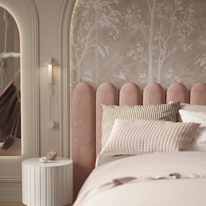 Op de afbeelding: Een roze gestoffeerd hoofdbord met een decoratief, gebogen ontwerp. Het hoofdbord bevindt zich tegen een muur met een beige behang met een wit boomsilhouetpatroon. Het bed heeft een wit dekbed, een gestreept kussen en een gestikt kussen.
