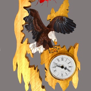 Könnte beinhalten: Eine Wanduhr aus Holz mit einem geschnitzten Adlermotiv. Der Adler ist in Braun, Weiß und Schwarz bemalt. Das Zifferblatt der Uhr ist weiß mit schwarzen römischen Ziffern und schwarzen Zeigern. Eine rote Ameise ist über dem Adler geschnitzt.