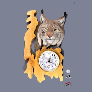 Puede incluir: Un reloj de pared de madera con una cabeza de lince tallada y una esfera redonda con números romanos. El reloj está pintado en tonos marrones y beige.