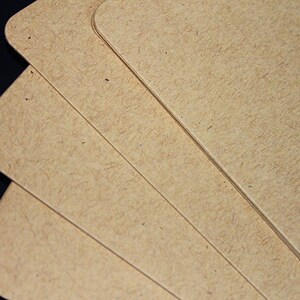 May include: Close-up of several light brown, rounded-corner cards. The cards have a textured surface and are stacked slightly, revealing their edges. The background is dark, creating contrast with the cards.