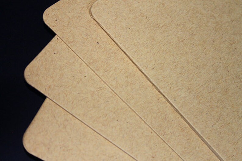May include: Close-up of several light brown, rounded-corner cards. The cards have a textured surface and are stacked slightly, revealing their edges. The background is dark, creating contrast with the cards.