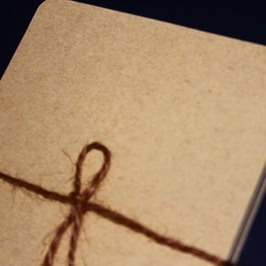 May include: A stack of rectangular, light brown cards tied with a dark brown twine. The twine is wrapped around the cards and tied in a simple bow. The cards have rounded corners.