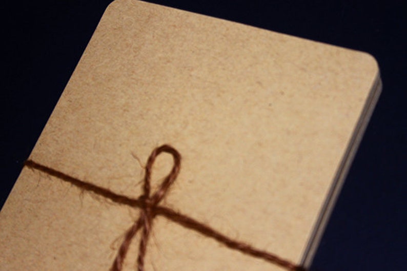 May include: A stack of rectangular, light brown cards tied with a dark brown twine. The twine is wrapped around the cards and tied in a simple bow. The cards have rounded corners.