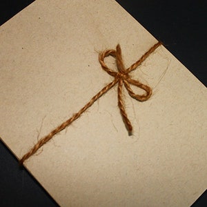 May include: A rectangular, light brown paper envelope tied with a brown twine bow. The envelope is angled, with a dark background. The twine is wrapped around the envelope and tied in a bow.