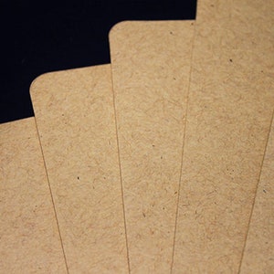 May include: A close-up of several rectangular, light brown cards with rounded corners. The cards have a textured surface and are arranged in a fan shape against a dark background. The cards appear to be made of a fibrous material.