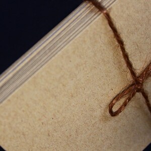 May include: Close-up of a stack of light brown paper cards tied with brown twine. The edges of the cards are visible, showing a layered effect. The twine is knotted in the center, creating a rustic and natural aesthetic.