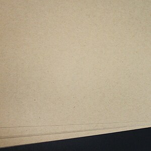 May include: A stack of beige-colored paper sheets. The paper has a slightly textured surface and appears to be a natural, uncoated material. The edges of the paper are visible, showing the layered arrangement.