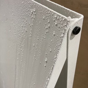 May include: A white metal surface with condensation droplets forming on it. The surface is part of a larger structure, possibly a shelf or a piece of furniture.