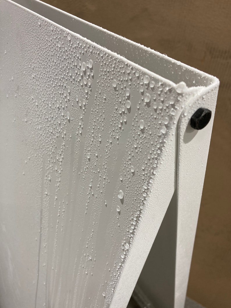 May include: A white metal surface with condensation droplets forming on it. The surface is part of a larger structure, possibly a shelf or a piece of furniture.