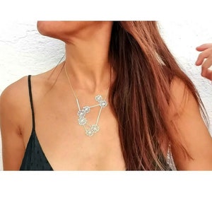 May include: A silver necklace with a geometric design featuring multiple interconnected circles. The necklace is worn by a person with long brown hair.