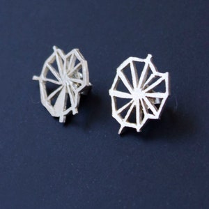 May include: A pair of silver earrings with a geometric design. The earrings are shaped like a wheel with spokes radiating out from the center.