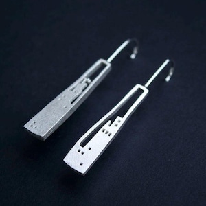 May include: A pair of silver earrings with a cityscape design. The earrings are long and slender, with a hook closure.