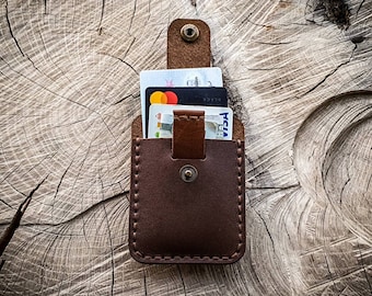 Könnte beinhalten: Ein brauner Lederkartenhalter mit Klappenverschluss und Druckknopf. Der Halter ist mit Kreditkarten gefüllt.