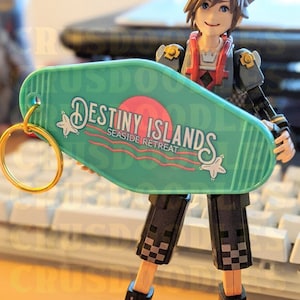 May include: A figurine of a character holding a teal motel-style keychain. The keychain reads "Destiny Islands Seaside Retreat" in white and red text. The character is wearing a black and gray outfit with a red vest.