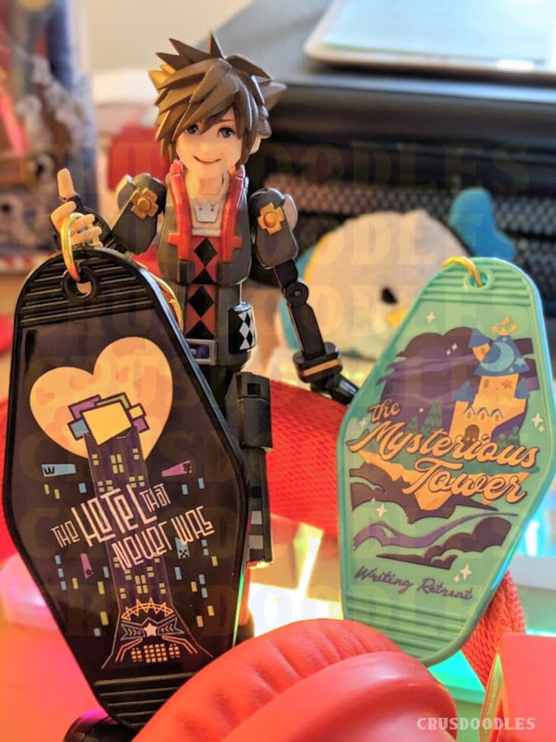May include: A figurine of a character from the Kingdom Hearts video game series holding two keychains. One keychain is black with the text "The Hotel That Never Was" and the other is green with the text "The Mysterious Tower".