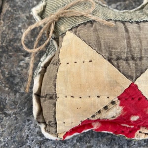 May include: A handmade patchwork heart-shaped pillow with a brown twine bow. The pillow is made of various fabrics, including beige, brown, and red with white polka dots.