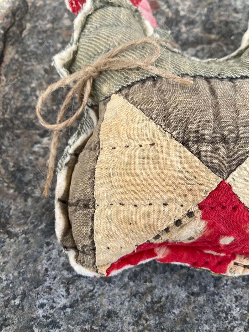 May include: A handmade patchwork heart-shaped pillow with a brown twine bow. The pillow is made of various fabrics, including beige, brown, and red with white polka dots.