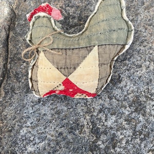 May include: A handmade quilted chicken toy with a red, white, and brown patchwork design. The chicken is made of fabric and has a rustic, vintage look.