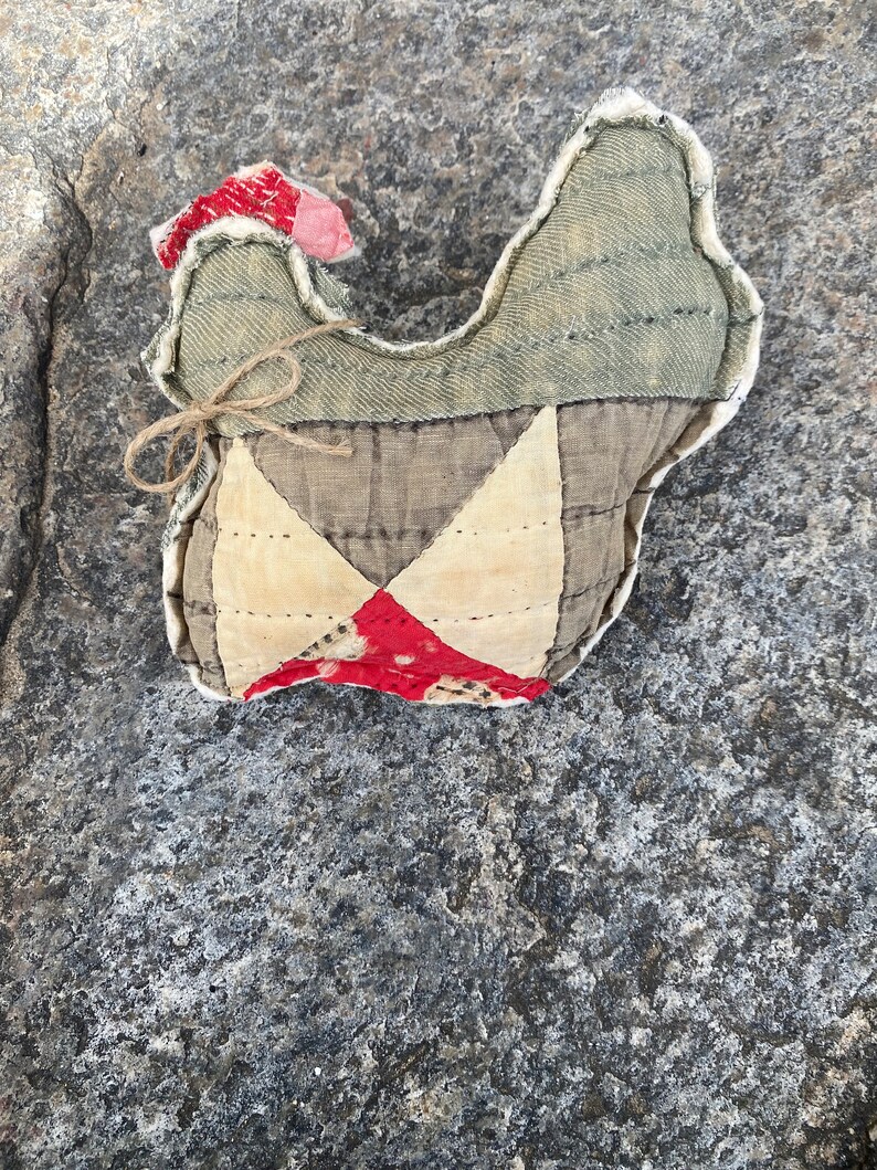May include: A handmade quilted chicken toy with a red, white, and brown patchwork design. The chicken is made of fabric and has a rustic, vintage look.