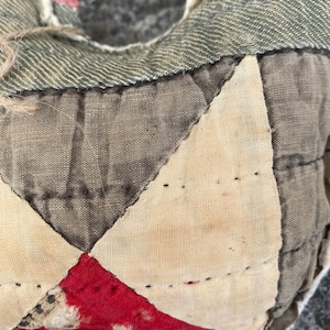May include: Close-up of a patchwork quilt made from different fabrics in shades of brown, white, and red. The quilt is stitched together with a running stitch.