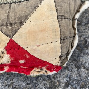 May include: Close-up of a patchwork quilt with a red, white, and gray pattern. The quilt is made of different fabrics and has been stitched together by hand. The quilt is worn and faded, showing signs of age.