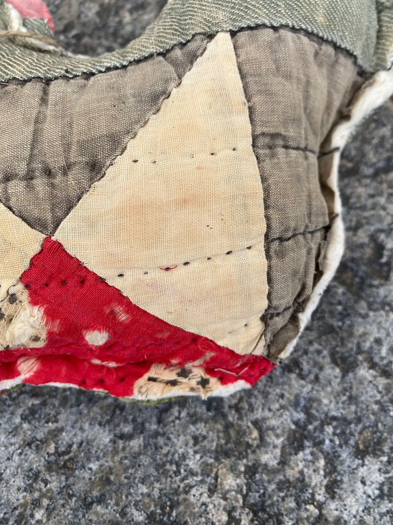May include: Close-up of a patchwork quilt with a red, white, and gray pattern. The quilt is made of different fabrics and has been stitched together by hand. The quilt is worn and faded, showing signs of age.