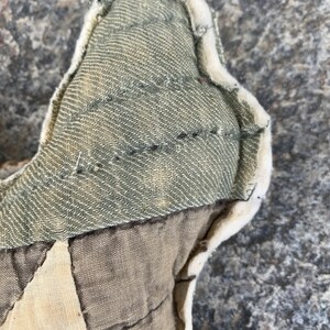 May include: Close-up of a handmade patchwork pillow with a green fabric panel and a white, fluffy trim. The pillow is made of different fabrics and has a quilted design.
