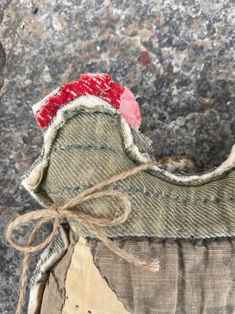 May include: A handmade fabric doll with a green denim bodice, a brown twine bow, and a red and white patchwork fabric head.