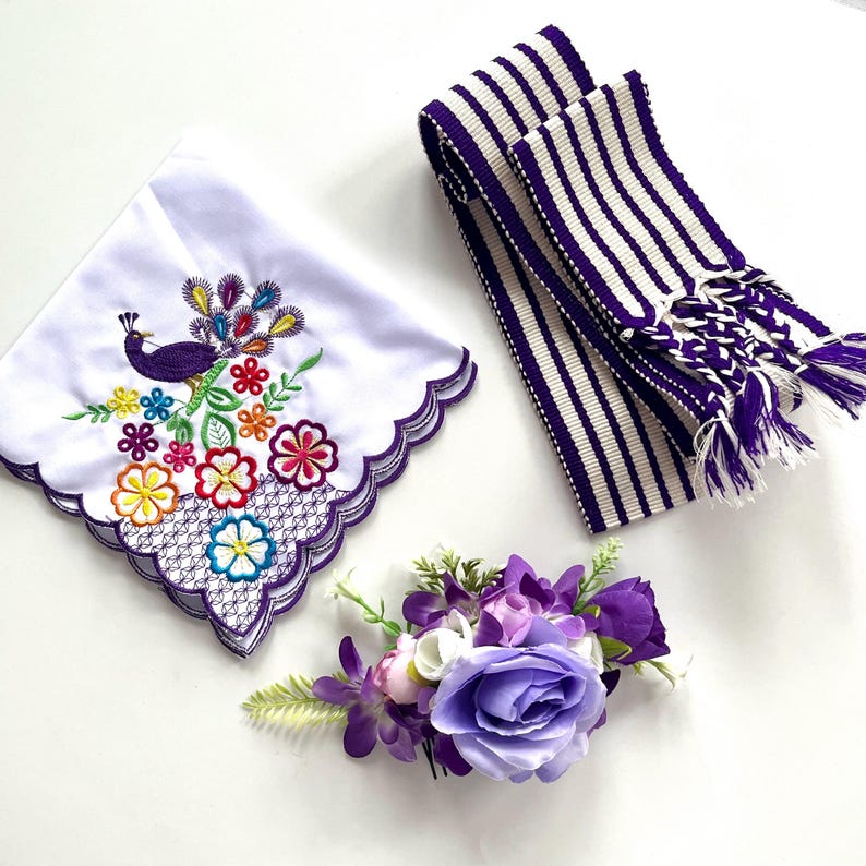 May include: A white handkerchief with a purple peacock and floral embroidery, a purple and white striped belt, and a purple floral hair comb. The handkerchief has a scalloped edge.