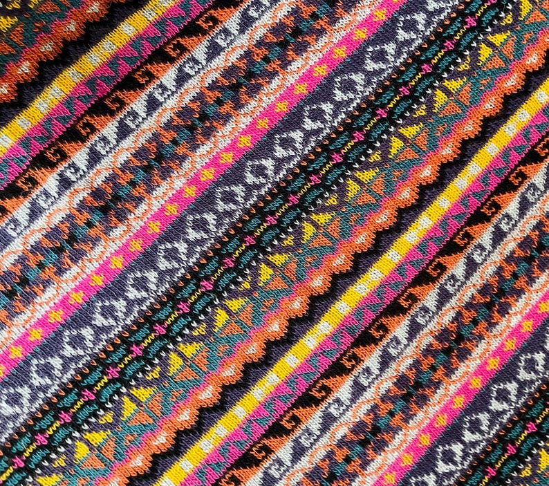 K&ouml;nnte beinhalten: Nahaufnahme eines farbenfrohen Textils mit diagonalem Streifenmuster. Das Design zeigt B&auml;nder in Pink, Gelb, Orange, T&uuml;rkis und Lila mit geometrischen und tribal inspirierten Motiven. Der Stoff hat ein strukturiertes Aussehen.