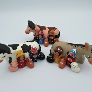 Könnte beinhalten: Eine Weihnachtskrippe mit einer schwarz-weißen Kuh, einem braunen Esel und einer Gruppe handbemalter Figuren. Die Figuren umfassen Maria, Josef, das Jesuskind und drei Könige.