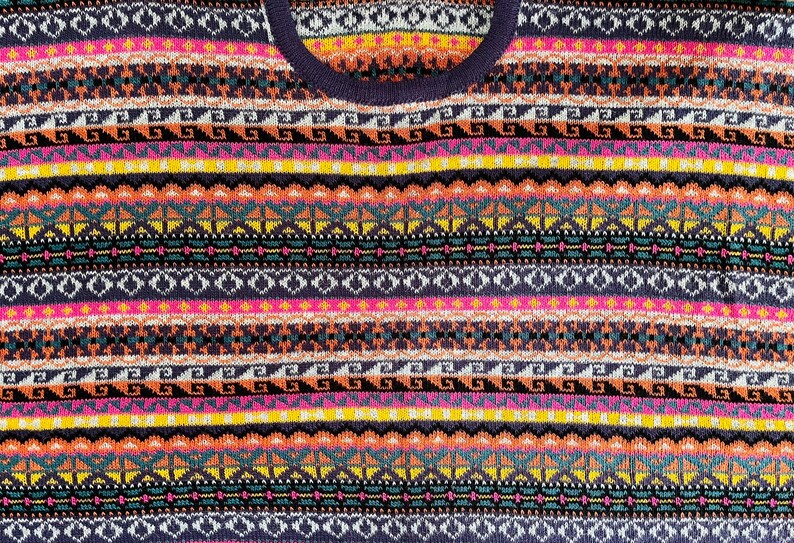 K&ouml;nnte beinhalten: Nahaufnahme eines farbenfrohen Pullovers mit geometrischem Muster. Der Pullover hat horizontale Streifen in verschiedenen Farben, darunter Pink, Gelb, Orange, T&uuml;rkis und Marineblau. Das Design umfasst Diamant- und Zickzackmuster.