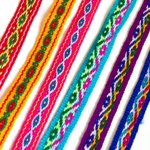 May include: Close-up of several colorful woven ribbons. The ribbons are in various colors, including red, yellow, pink, turquoise, purple, and blue. Each ribbon features a repeating geometric pattern in contrasting colors. The ribbons are arranged diagonally.