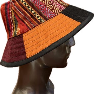 以下が含まれることがあります： カラフルな幾何学模様のついたバケットハット。帽子は織り生地で作られており、黒いつばがあります。