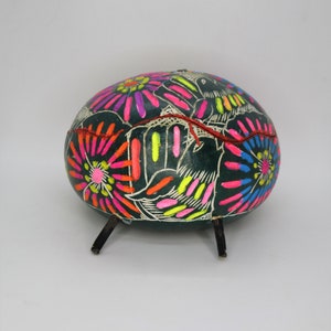 Può includere: Una zucca dipinta a mano con sfondo nero e motivi floreali colorati. La zucca ha tre gambe ed è un pezzo tradizionale di arte popolare messicana.