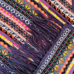 K&ouml;nnte beinhalten: Nahaufnahme eines farbenfrohen Strickschals mit geometrischem Muster. Der Schal weist eine lebendige Mischung aus Farben auf, darunter Lila, Rosa, Orange, Gelb und Wei&szlig;. Der Schal hat einen Fransen aus lila Garn.