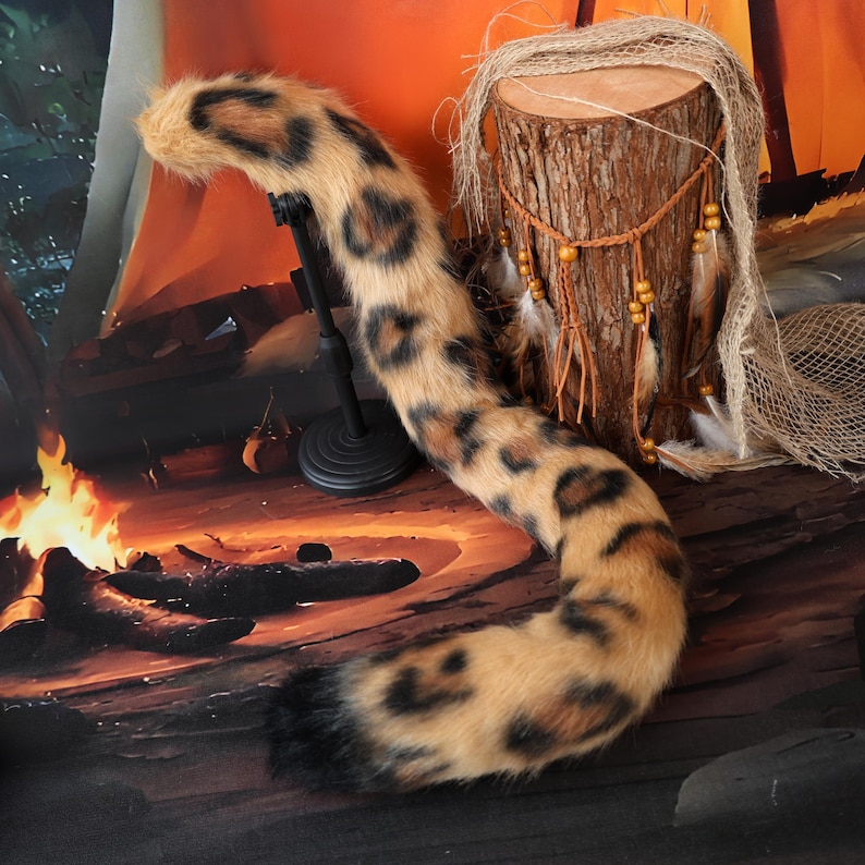 Puede incluir: Una larga cola de piel sint&eacute;tica afelpada con una base de color tostado y manchas de estampado de leopardo en marr&oacute;n oscuro y negro. La cola tiene una punta negra s&oacute;lida y est&aacute; montada sobre un soporte de metal negro.