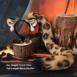 Puede incluir: Un conjunto que incluye una diadema negra con orejas de animal de piel sint&eacute;tica y una cola larga a juego de piel sint&eacute;tica con estampado de leopardo. Las orejas miden 7 cm de alto y la cola 90 cm de largo, seg&uacute;n el texto de la imagen.