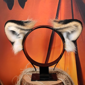 Puede incluir: Una diadema negra con dos orejas de animal de piel sint&eacute;tica. Las orejas tienen un patr&oacute;n de color degradado con puntas negras, secciones centrales de color tostado y detalles de pelo blanco en la parte interna de la oreja.